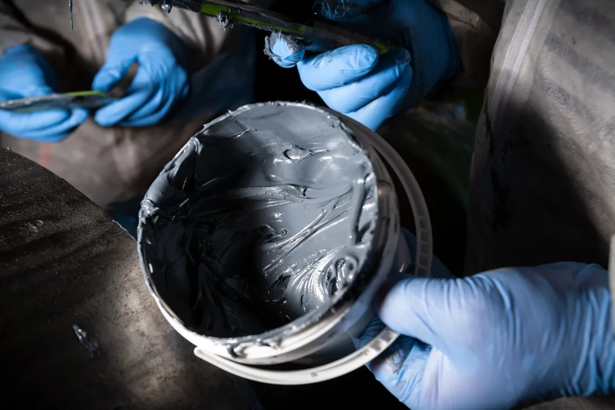 Gloved workers mixing epoxy in a container before a composite pipe repair.