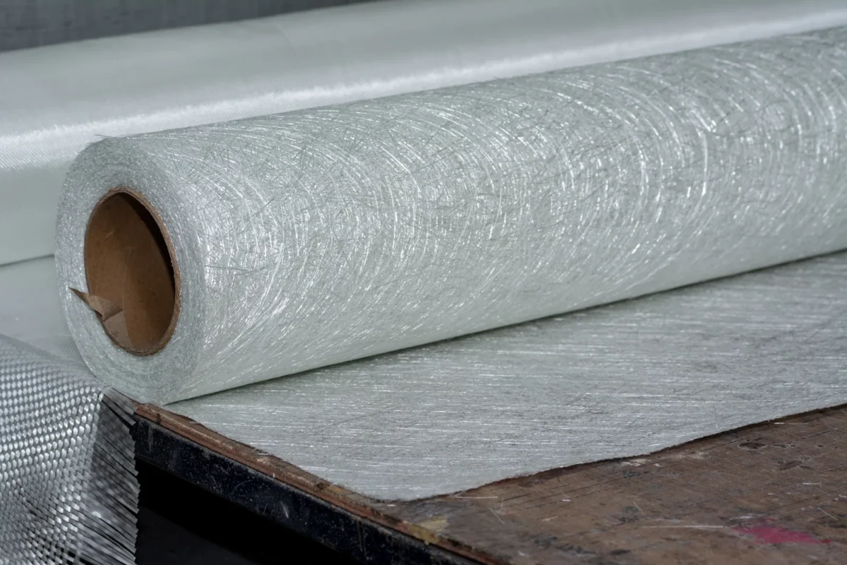 A roll of glass-fibre reinforcement mat laid out on a workbench.